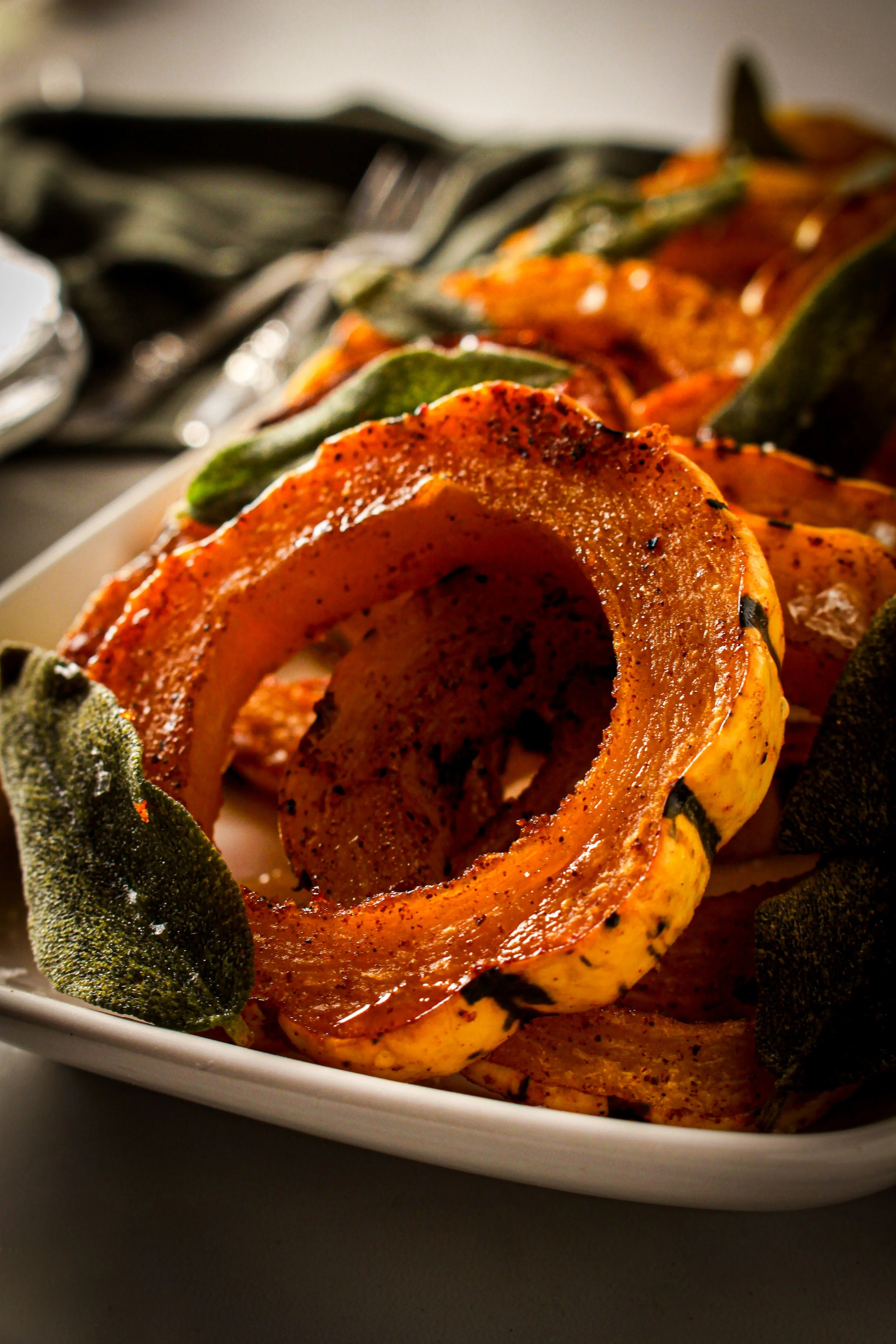 Close-up of roasted acorn squash rings and sage leaves on a white plate