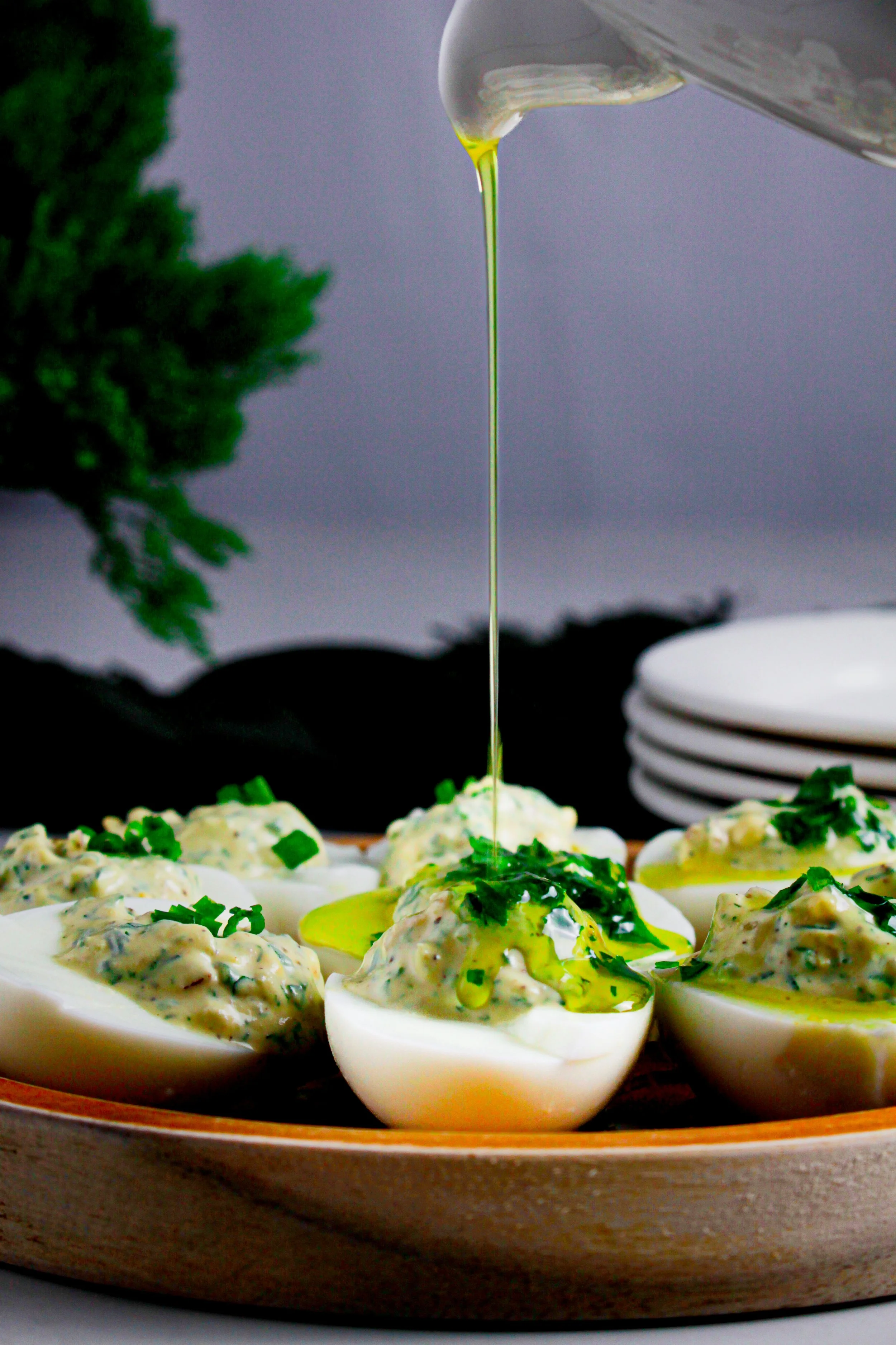 Deviled eggs topped with green herbs, with green oil being drizzled on top